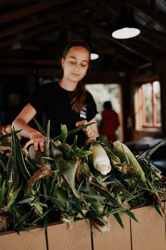 Fille du propriétaire de la Ferme Degau tenant du maïs sucré devant le kiosque à Neuville au Québec.